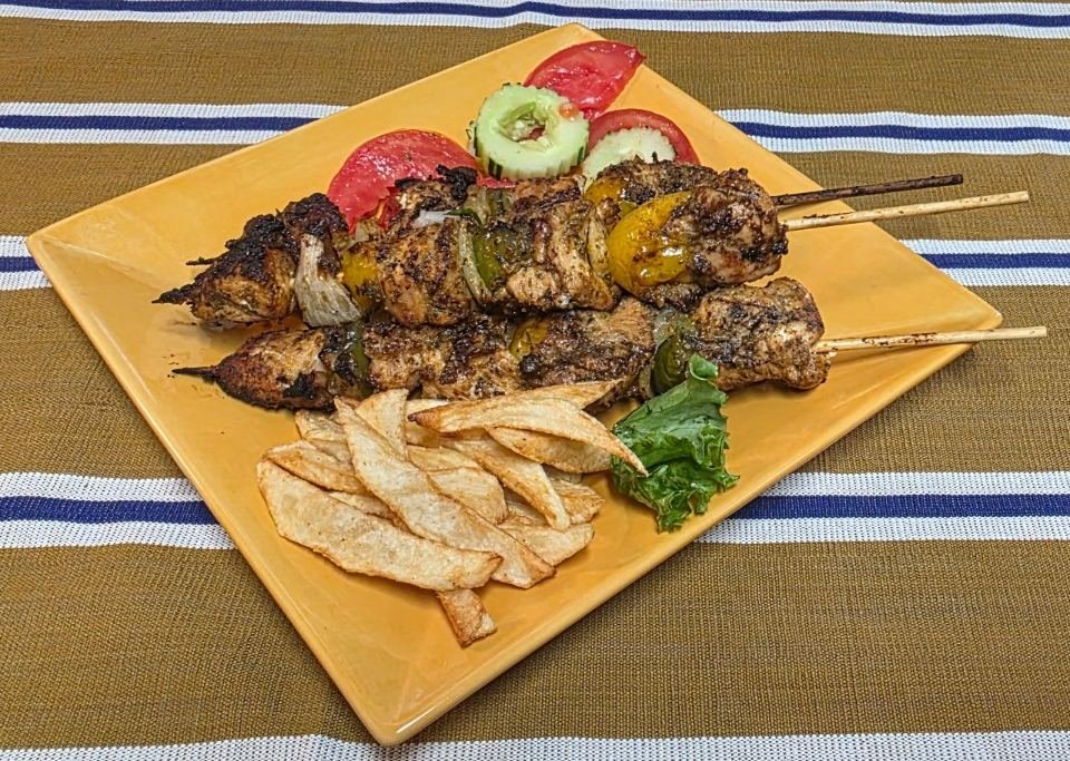 Charcoal-grilled chicken kabobs with peppers and onions, fries and fresh tomato on a yellow plate