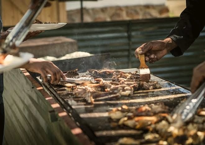 Cooks basting and turning meat on a large outdoor grill